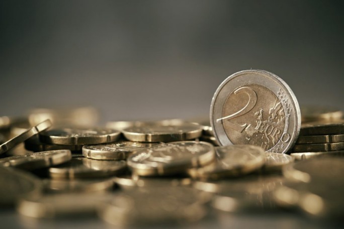 A detailed view of multiple Euro coins with a prominent 2 Euro coin standing upright. The coins are scattered on a flat surface, creating a metallic and textured visual. The setting emphasizes financial themes and currency details.