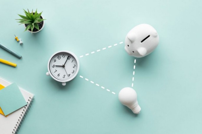 A white piggy bank, an analog clock showing 10:10, and a light bulb are arranged on a pastel blue background. The items are connected with dotted lines, symbolizing ideas of time, savings, and energy. A small potted plant, stationery, and a notebook add to the minimalistic composition.